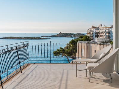 Modern balkong med grå stolar och panoramautsikt över ett blått hav med öar och kustbebyggelse.