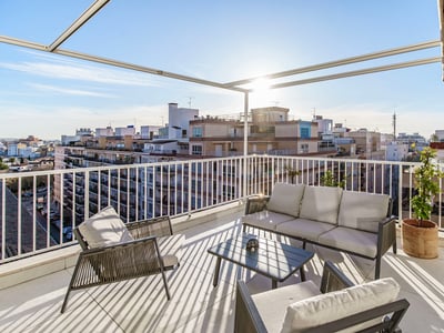 Terraza soleada con muebles grises modernos, barandilla blanca y amplias vistas al horizonte urbano.