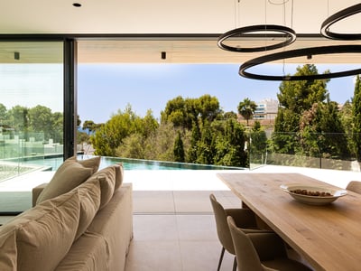 Heller Wohnbereich mit beigem Sofa und direktem Zugang zu einer Terrasse mit Infinity-Pool und Grünblick.