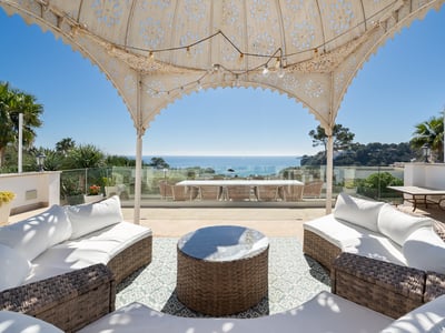 Spacious terrace with wicker sofas under a decorative gazebo overlooking the Mediterranean sea.