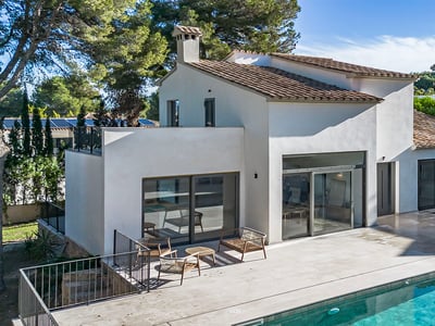 Modern white villa with a terracotta roof, large glass doors, and a stone terrace next to a turquoise swimming pool.