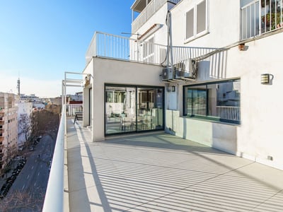 Terraza soleada con suelo de baldosas claras, barandillas blancas y vistas a una calle de la ciudad bajo un cielo azul.