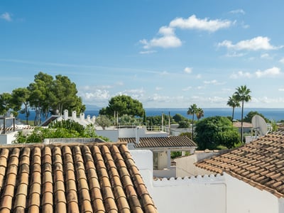 Vue surélevée de toits en terre cuite, de murs blancs et de palmiers avec la mer bleue en arrière-plan.
