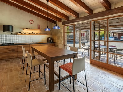 Cocina con vigas de madera, suelo de terracota y puertas de cristal que dan a un patio exterior.
