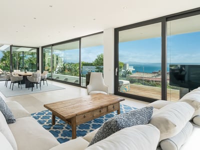 Salon spacieux avec canapés blancs, table basse en bois et grandes baies vitrées s'ouvrant sur une terrasse vue mer.