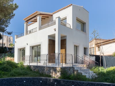 Vit modern tvåvåningsvilla med naturstenssockel och takpannor under en klarblå himmel.