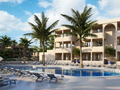 Large blue swimming pool with grey loungers, umbrellas, and palm trees in front of a modern beige building with balconies.