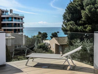 Tumbona blanca en terraza moderna con barandilla de cristal y vistas al mar Mediterráneo.