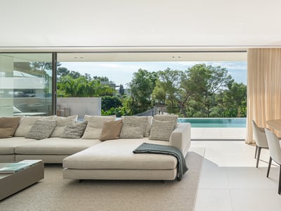 Elegante salón moderno con sofá beige, comedor y grandes ventanales que dan a una terraza con piscina y árboles.