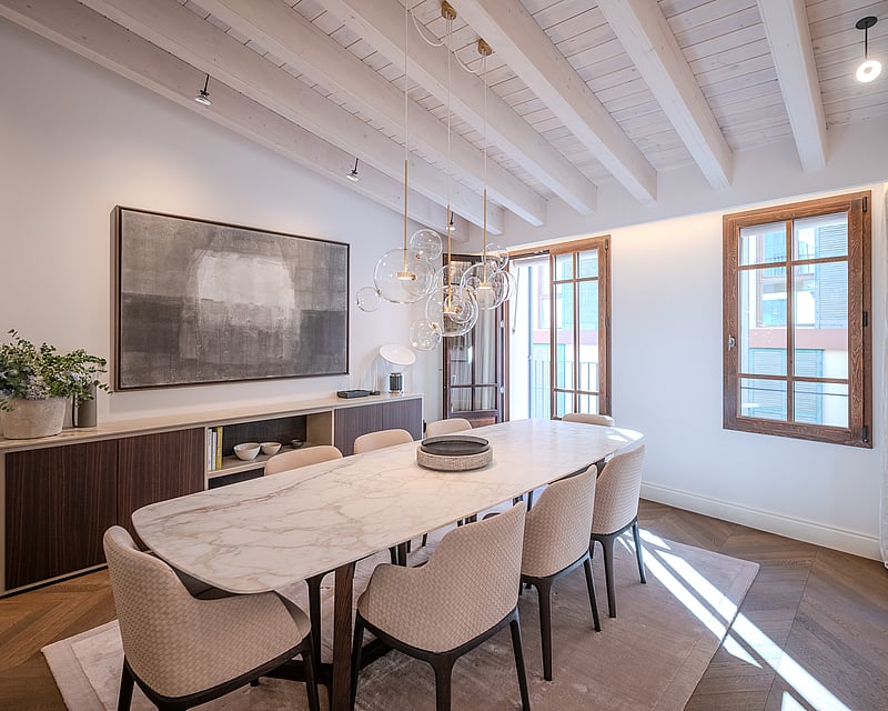 Modern dining room with a marble table, textured chairs, glass bubble chandelier, and whitewashed wooden beam ceiling.