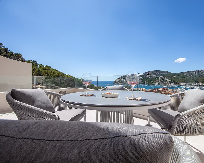 Modern terrace table with two glasses of wine set against a spectacular view of the harbor and sea under a clear blue sky.