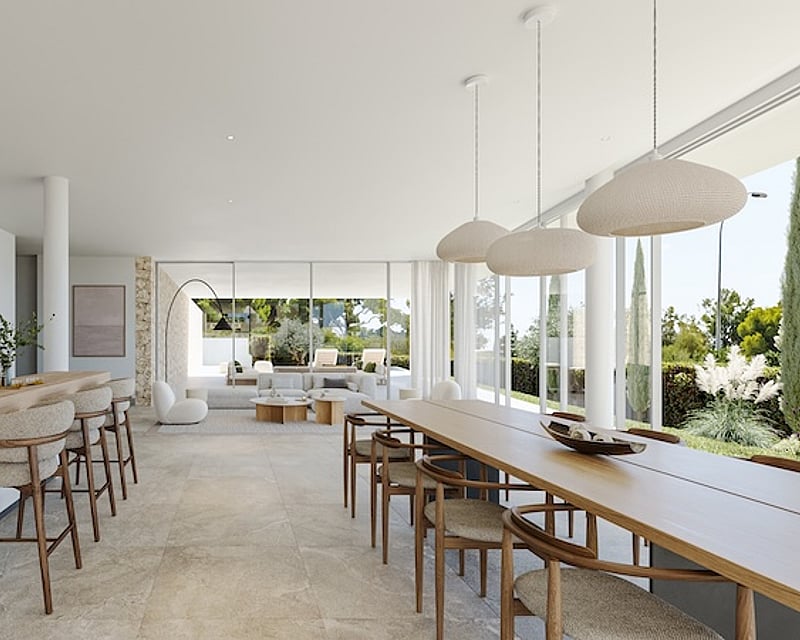 Vista amplia de una cocina blanca minimalista y zona de comedor con grandes ventanales hacia un jardín soleado.