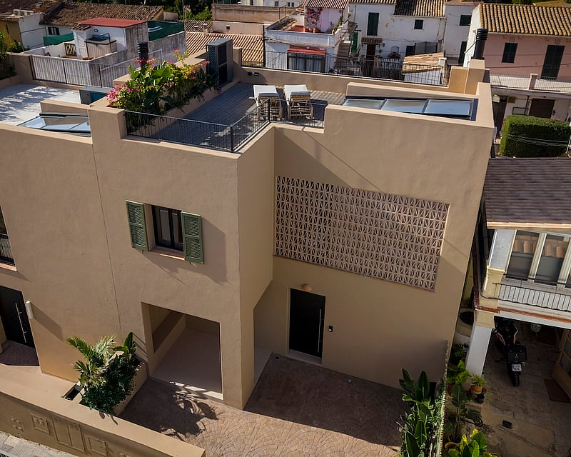 Aerial view of a modern ochre villa featuring a rooftop terrace, green shutters, and decorative lattice stonework.