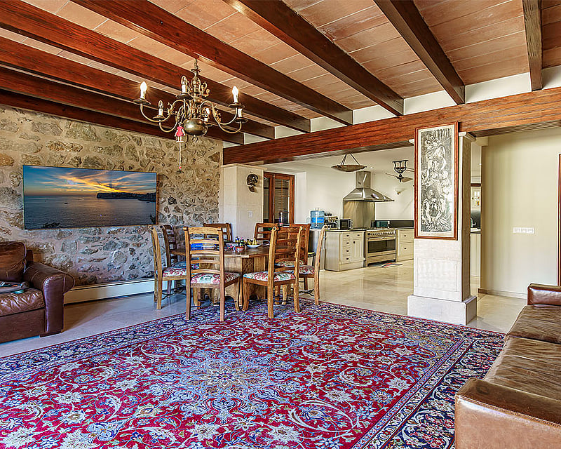 Open plan living room with exposed wood beams, stone wall, leather seating, and a dining area leading to a kitchen.