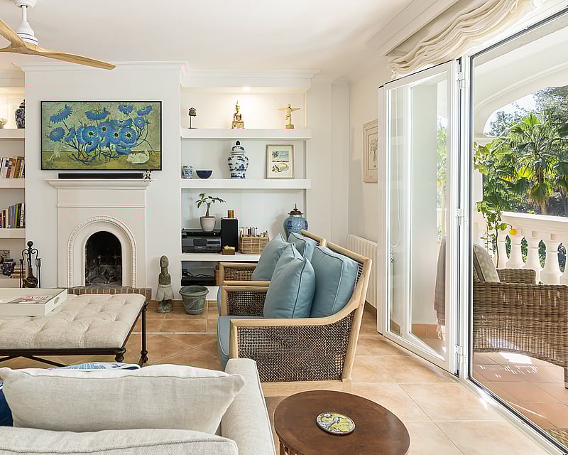Bright living room with terracotta floors, white fireplace, built-in shelves, and glass doors opening to a lush terrace.