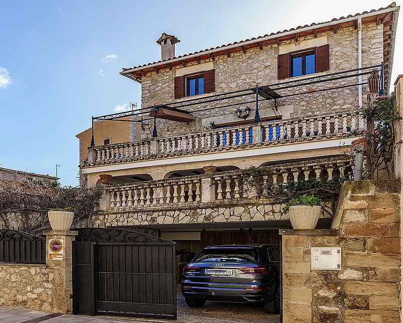 Three-story traditional stone house with terracotta roof, multiple balustraded terraces, and an integrated garage entrance.