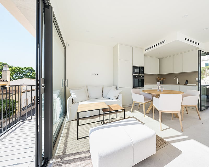 Bright open-plan living and dining room with white furniture, integrated kitchen, and floor-to-ceiling glass doors.