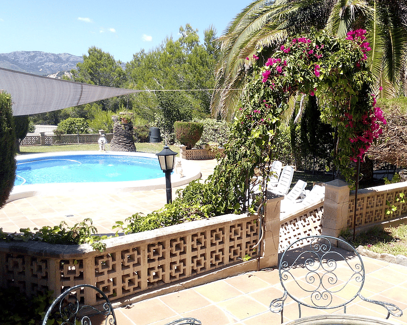Terraza soleada con piscina circular, baldosas de terracota, un arco de buganvillas y montañas al fondo.