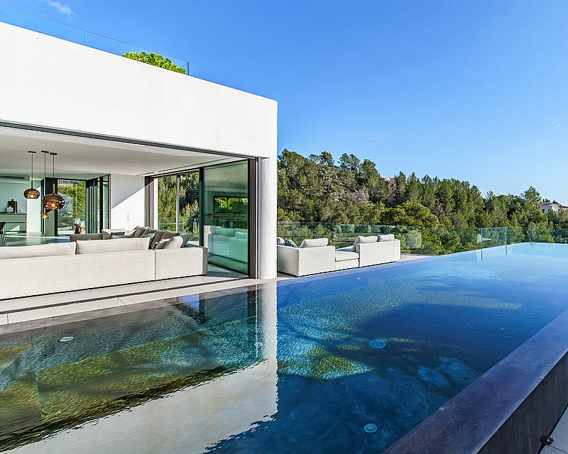 Luxury villa with infinity pool, glass terrace, and modern lounge overlooking a lush green forest.