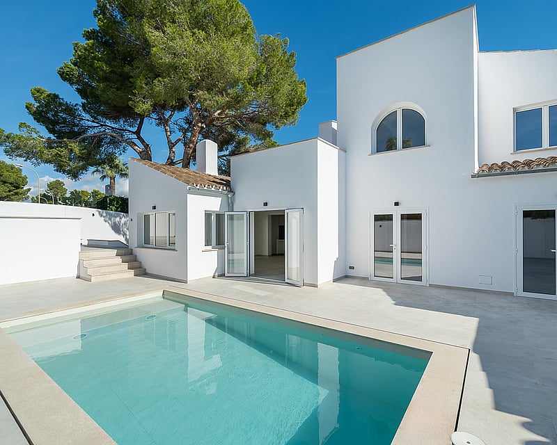 Modern white villa featuring a rectangular swimming pool and sun-drenched terrace under a clear blue sky.