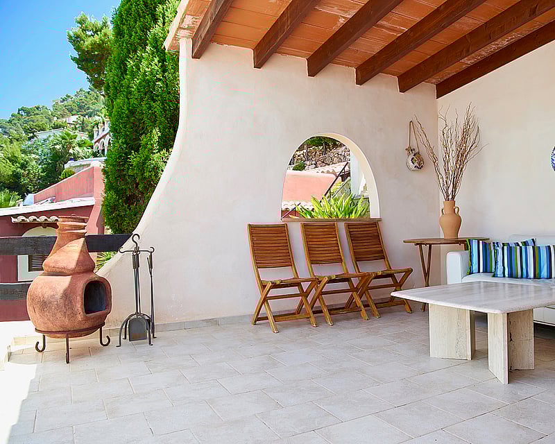 Covered terrace featuring white sofas, marble table, terracotta fireplace, and exposed wooden beams.