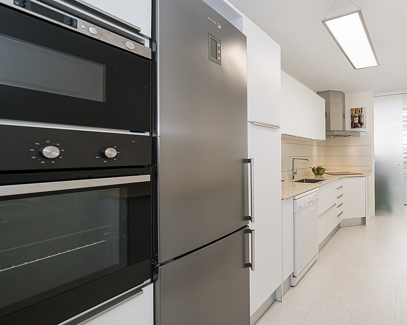A modern galley-style kitchen with white cabinetry and stainless steel appliances.
