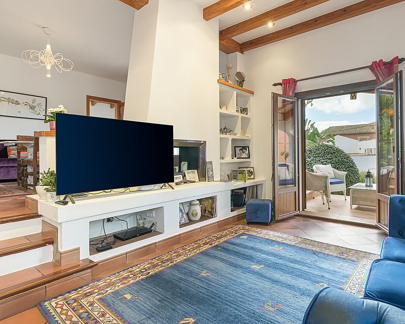 Living room featuring terracotta floors, exposed wooden beams, and open French doors leading to a sunlit terrace.