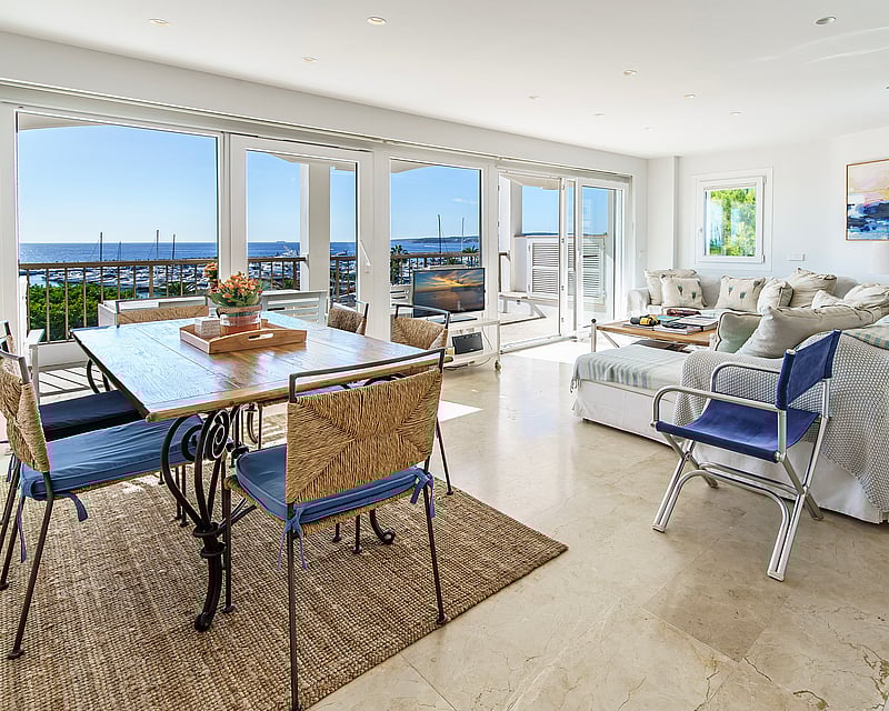 Open-plan living room with marble floors and large windows overlooking a marina and sea.