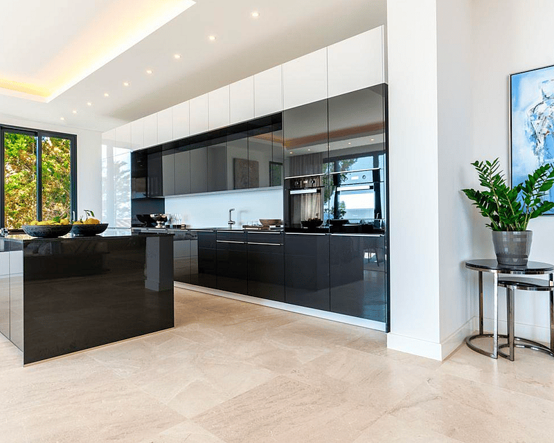 Spacious modern kitchen featuring a large black glossy island, dark cabinetry, and light stone flooring.