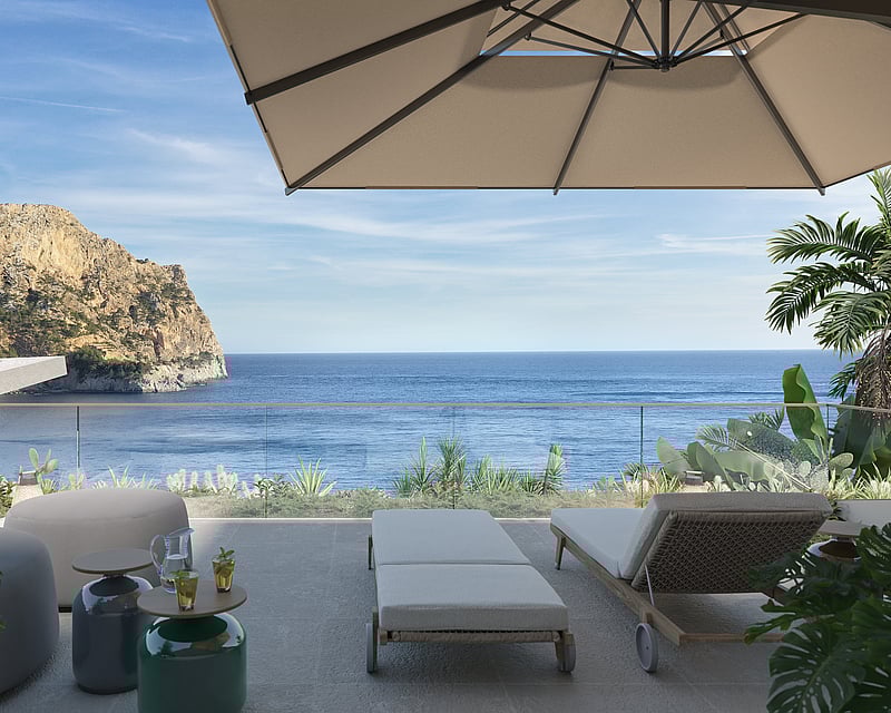 A sunny terrace with sun loungers, a parasol, and a glass railing overlooking the Mediterranean sea and a rocky cliff.