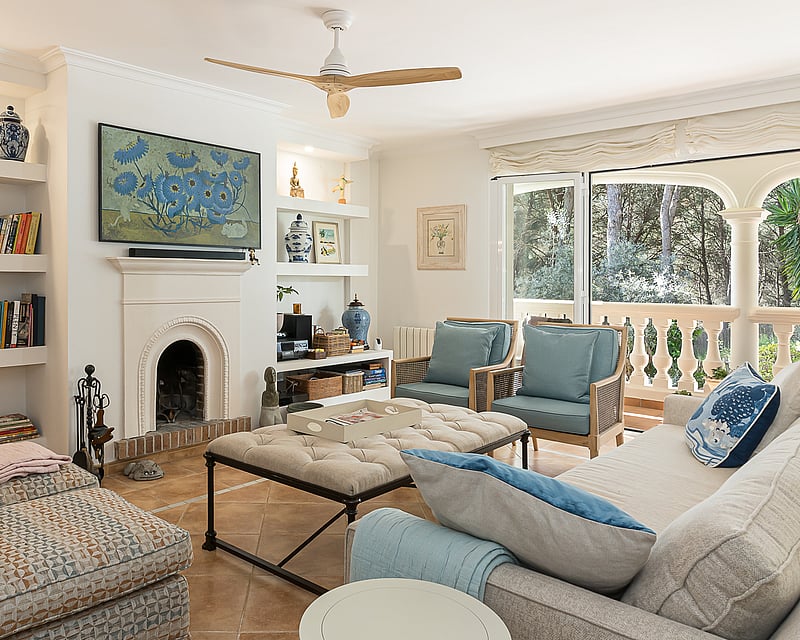 Bright living room featuring a white arched fireplace, built-in shelving, blue armchairs, and glass doors to a terrace.