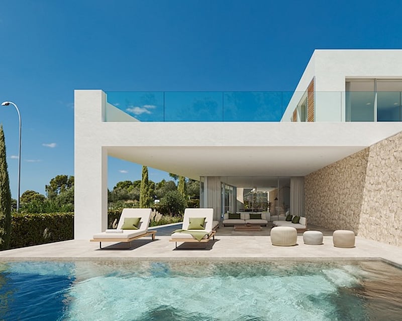 Vista de una piscina turquesa hacia una villa blanca moderna con terraza sombreada, pared de piedra y tumbonas.