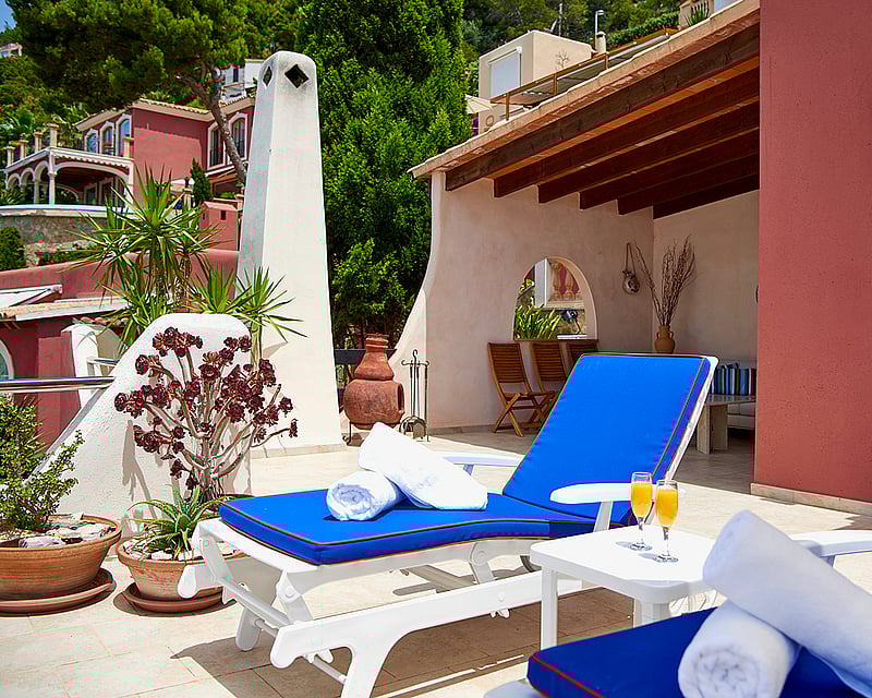 Sunny terrace featuring vibrant blue sun loungers, white towels, and a wooden-beamed porch.