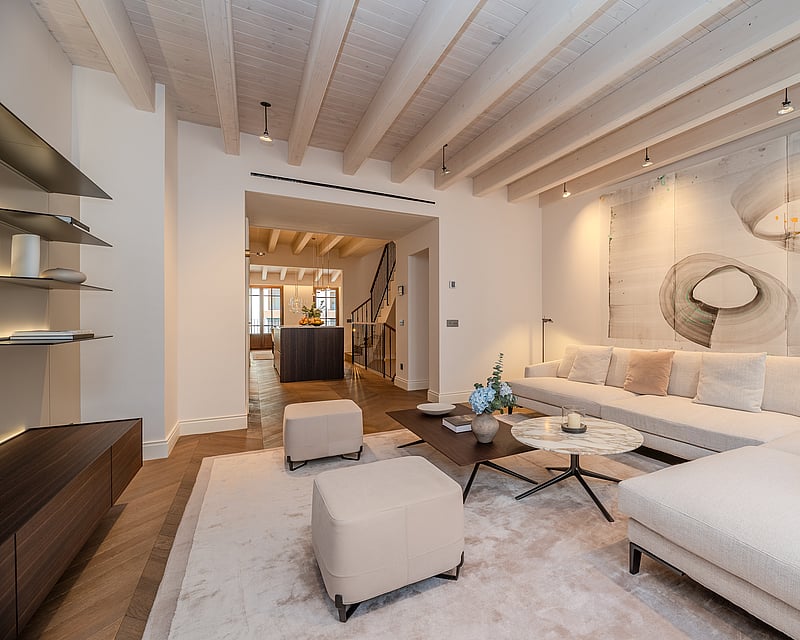 Modern living room featuring a cream sofa, marble coffee table, exposed wood ceiling beams, and herringbone floors.