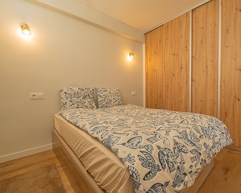 Dormitorio moderno con cama de textiles azules, armarios empotrados de madera de roble e iluminación de pared cálida.