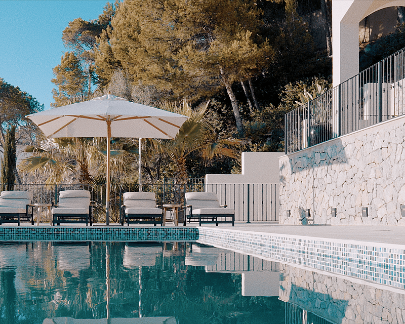 Infinity swimming pool with four sunbeds under a white umbrella, surrounded by stone walls and Mediterranean greenery.