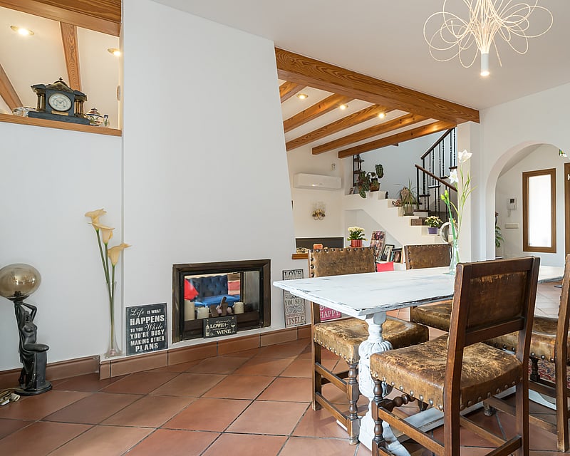 Interior dining room with terracotta floors, exposed wooden beams, white distressed table, and leather chairs.