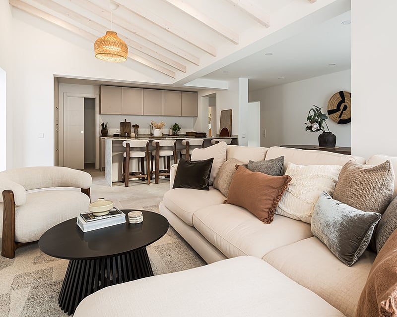 Bright living room with beige sofa, wooden ceiling beams, and a modern kitchen island in the background.