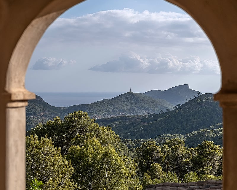 A view of lush green mountains and the distant sea framed by a traditional stone archway.