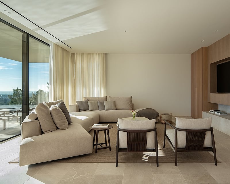Modern living room with a beige sectional sofa, wood paneled TV wall, and floor-to-ceiling windows with a scenic view.