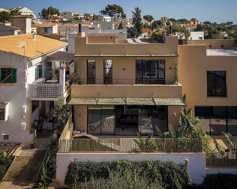 A modern ochre-colored multi-level villa facade with large black-framed windows and bamboo fencing under bright daylight.
