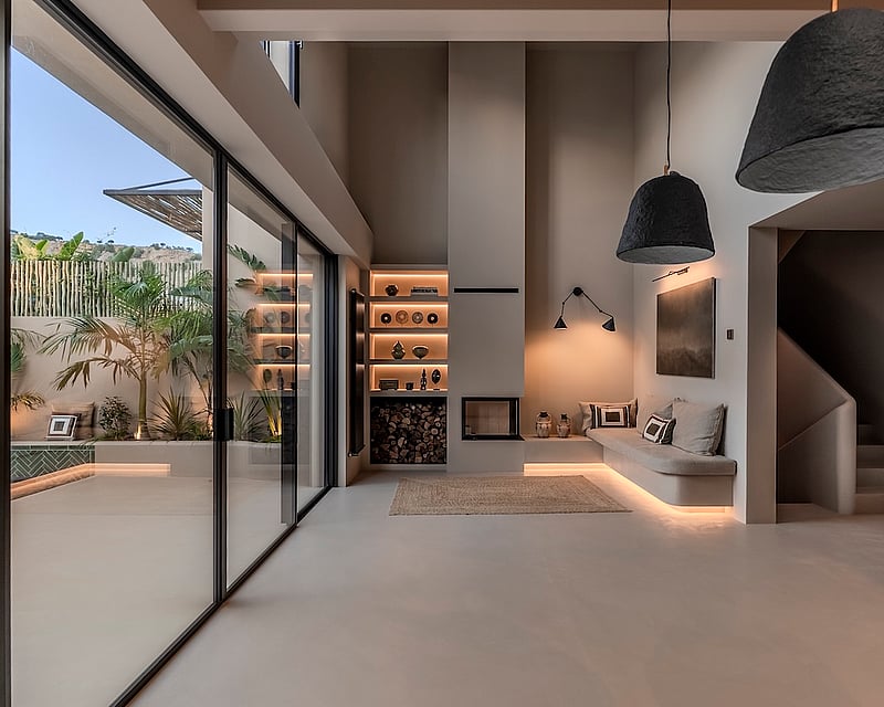 Minimalist living room with high ceilings, a built-in sofa, fireplace, and large glass doors opening to a tropical patio.