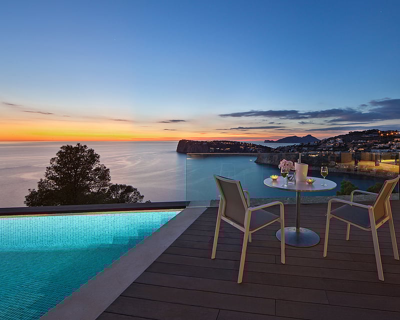 Luxury terrace with infinity pool, table for two, and panoramic sea view at sunset.