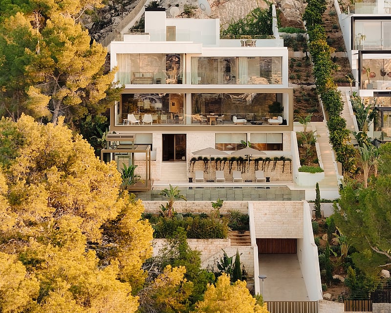 Contemporary three-story white villa built into a rocky hillside with large glass windows, pool, and terraced gardens.