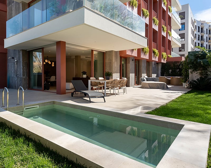 Luxury terrace with private plunge pool, outdoor dining set, sun lounger, and green lawn by a modern apartment building.