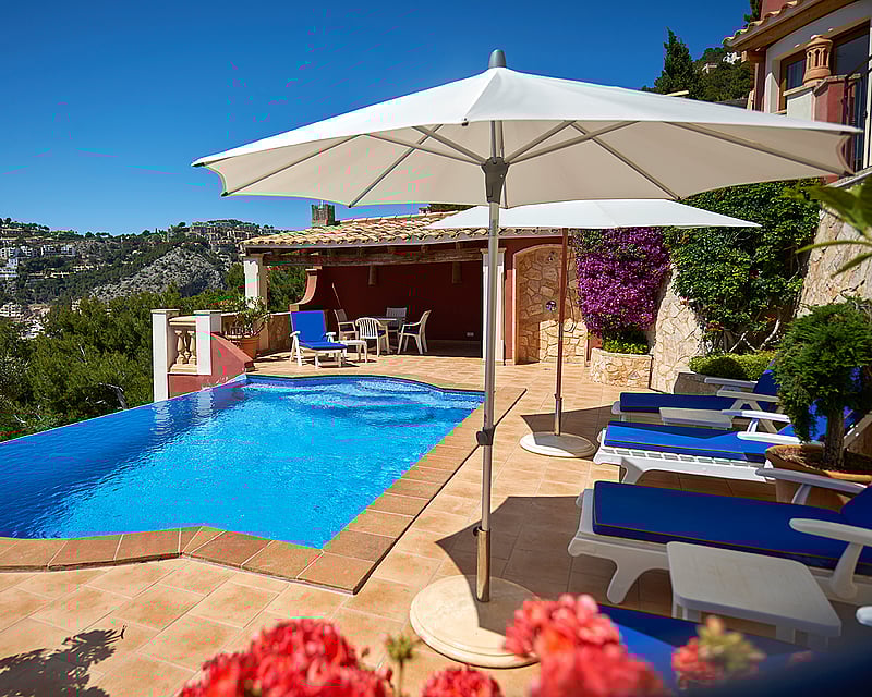 Private pool terrace with blue sun loungers and white umbrellas overlooking scenic hills and a bright blue sky.