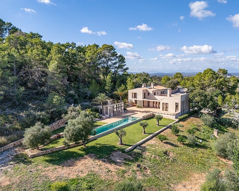 Aerial view of a luxury stone villa with a long turquoise pool surrounded by olive trees and lush forest.
