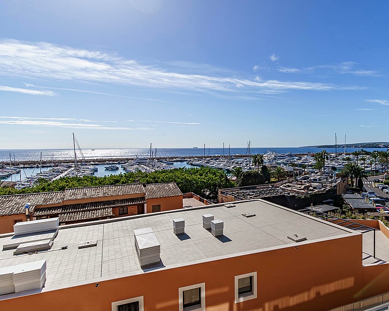 Elevated view overlooking a marina with yachts and the Mediterranean sea under a clear blue sky.