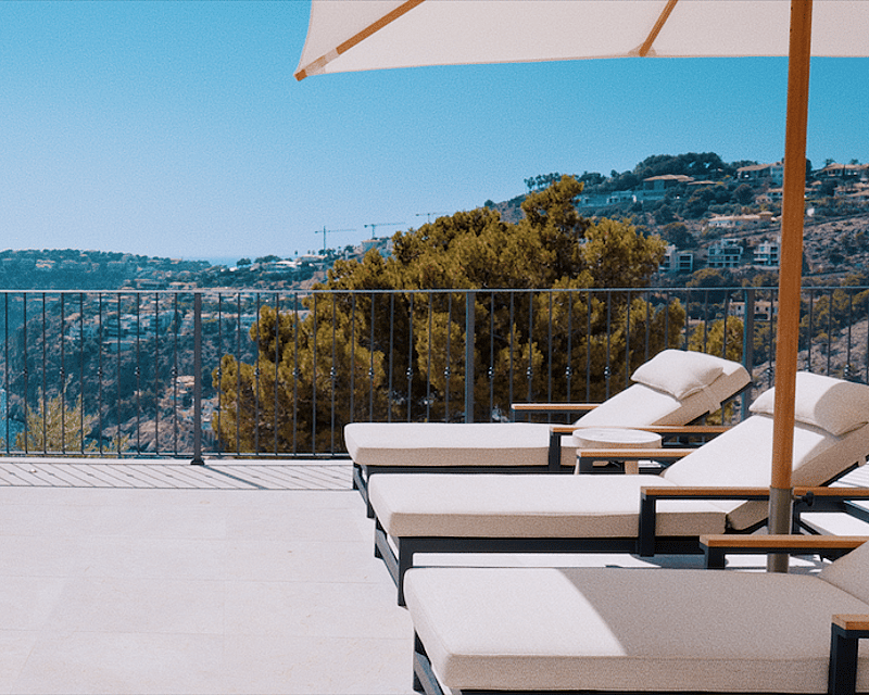 Luxury terrace featuring white sun loungers and a parasol next to an infinity pool overlooking the sea and cliffs.