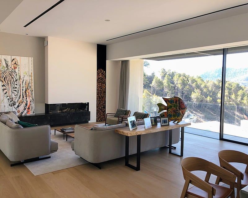Modern living room featuring floor-to-ceiling glass walls overlooking a forest, a sleek fireplace, and oak floors.